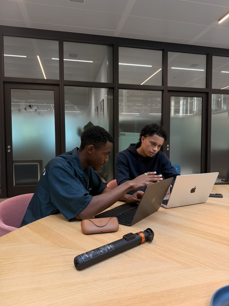 Two LDJ Marketing team members working together on laptops at a meeting table,
                a camera grip and lens case in front of them.